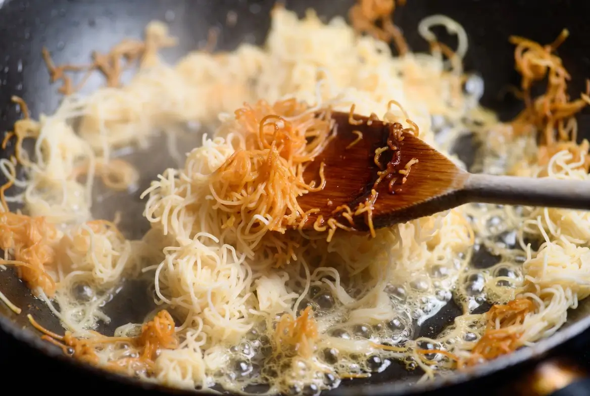 Chopped kataifi pastry frying in butter in a pan, transitioning from white to deep golden brown